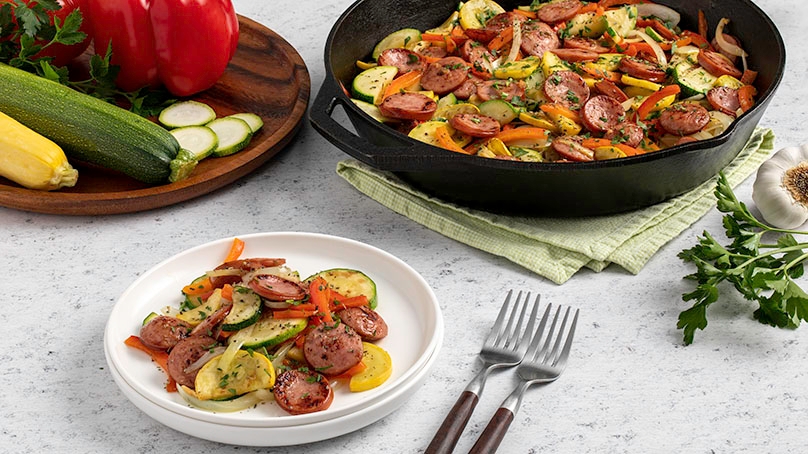 Smoked Sausage and Squash Skillet , cutt5ing board with fresh vegetables, skillet on kitchen towel, light wood table, forls, white plate