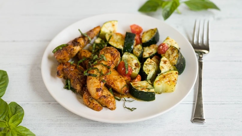 One Pan Balsamic Chicken and Veggies on white plate, fork ,basil, white wood table