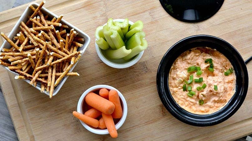 Light Slow Cooker Buffalo Chicken Dip in bowl, celelry stalks, carrots, pretzels, cutting board