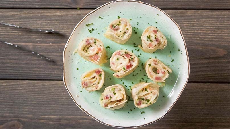 Smoked Ham Pinwheels on plate, dark wood table , serving tongs