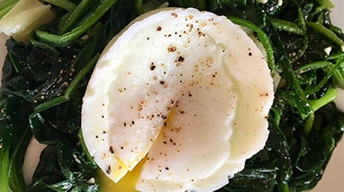 Poached egg on cooked greens in bowl