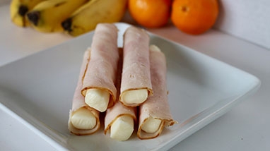 Protein wraps stacked on square white plate, white counter, bananas, oranges