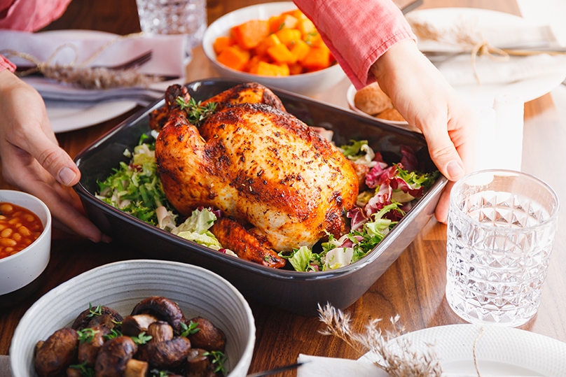 Hands put a dish with whole roasted chicken on a festive table