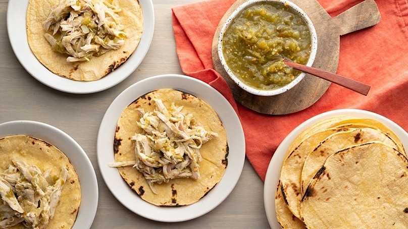 Easy Salsa Verde Chicken Tacos on plates, bowl of salsa on cutting board, red kitchen towel, wood table