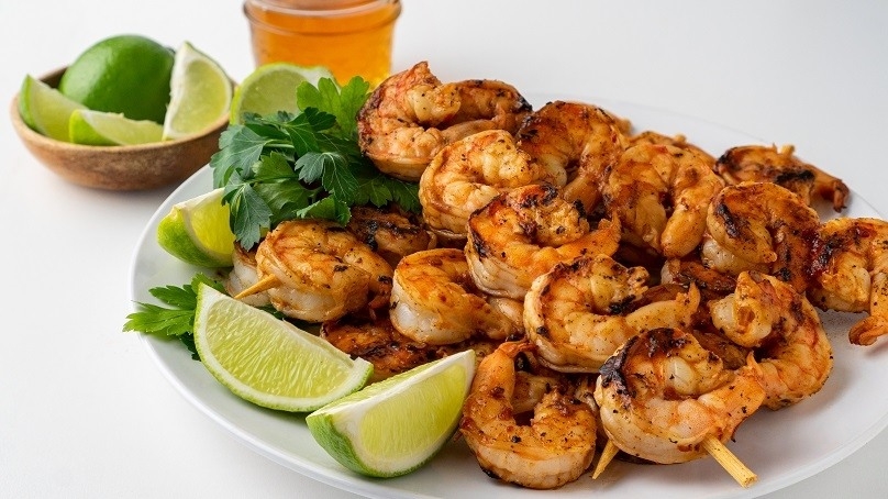 Sweet and Spicy Grilled Shrimp on skewers, white plate, celntro, lime wedges