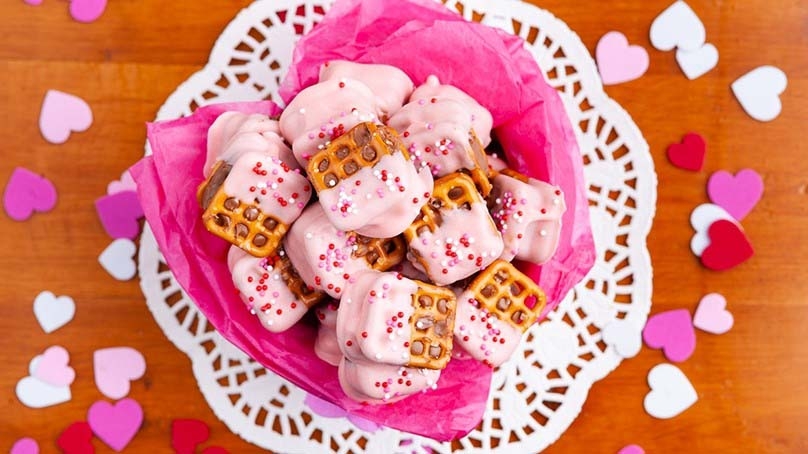 Candy Bar Pretzel bites in dish surrounded by cabdy hearts, doilie, wood table