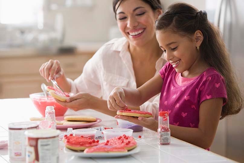 Mother and daughter decorating valentine's cookies and the kitchen table