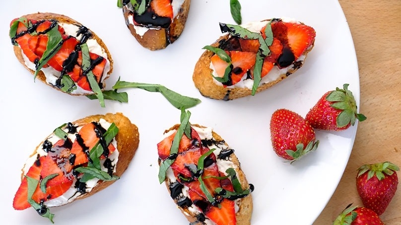 Strawberry Basil Bruschetta on white plate with fresh strawberries, wood table