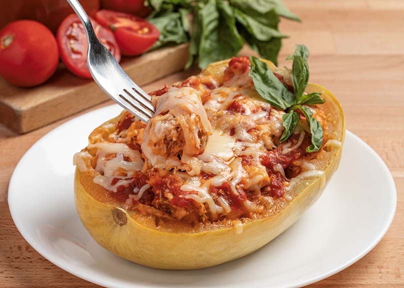 Keto Chicken Parmesan Stuffed Spaghetti Squash, white plate, fork, cutting board, tomatoes, basil, wood table