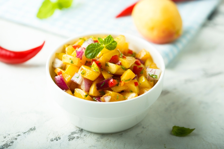 White bowl of cut up apricots, halves of apricots with blue checkerboard napkin in background, white stone counter