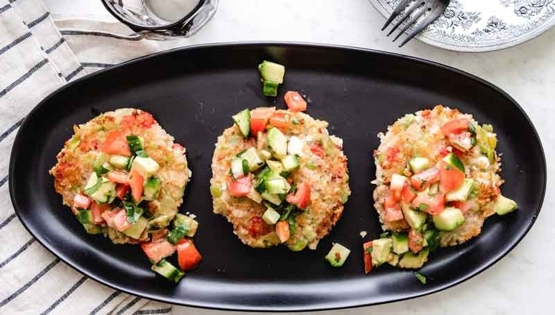 Butterbean cake topped with cucumber tomato salad on dark plate, fork, dinner napkin