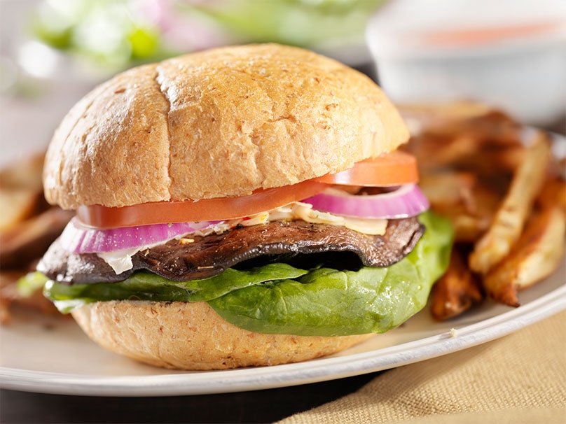 Portabella mushroom burger with spinach, red onions, tomato and cheese, with fries and sauce on plate