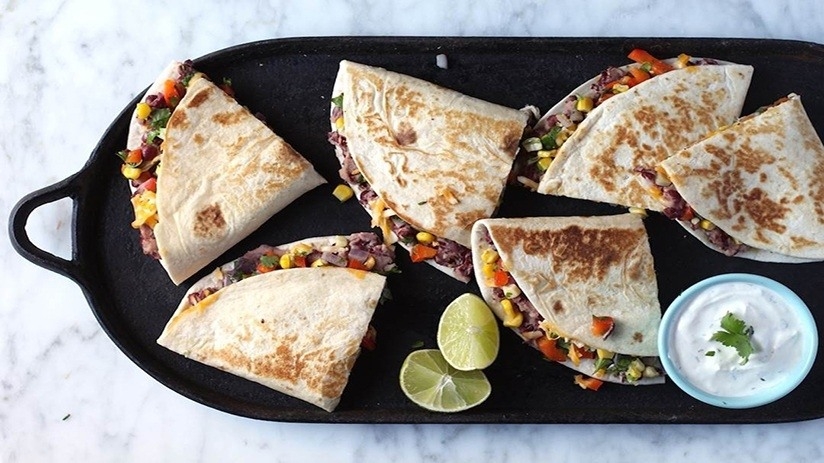 Southwest quesadillas with cilantro lime sour cream, cut lime, cup of cilantro sour cream on black serving dish, marble counter