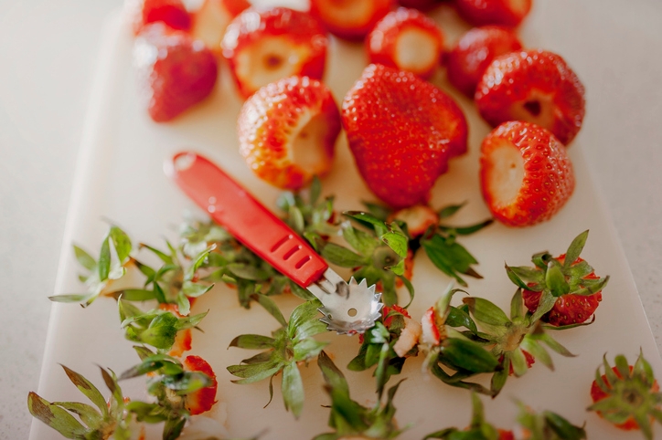 Strawberries with green tops removed, mellon baller, cutting board