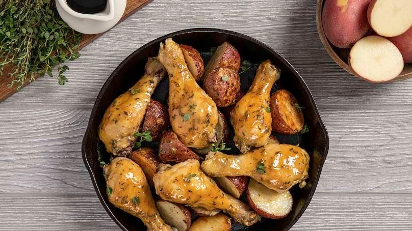 Top down of one-Pan maple-mustard roast chicken in cast iron pan, serving bowl of halved potatoes in background