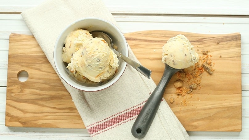 Five ingredient candy bar ice cream, ice cream scoop, white napkin with red stripe, cutting board on white wood table