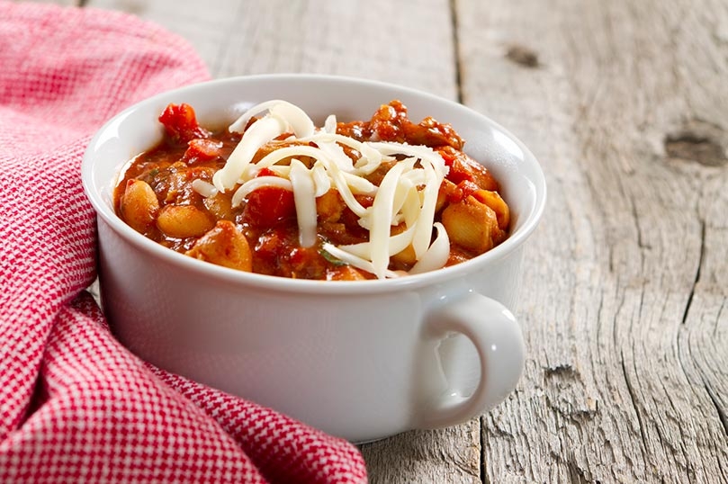 Cup of chicken and white bean chili with a plaid red napkin, wood table