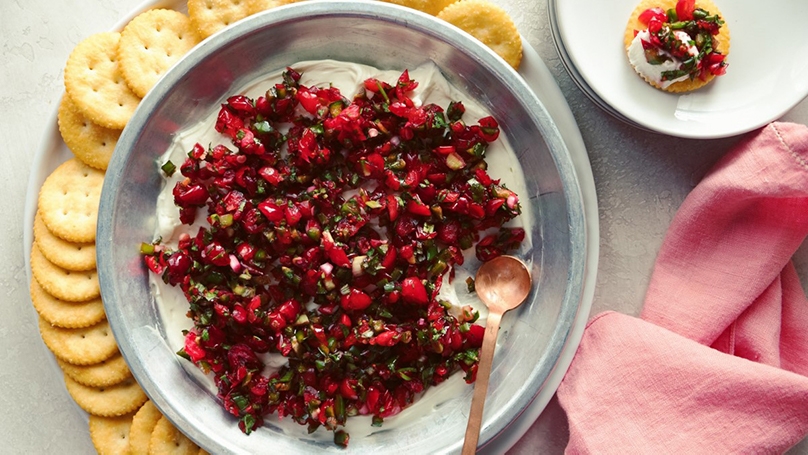 Cranberry jalapeno dip in serving dish with crackers, pink napkin in corner