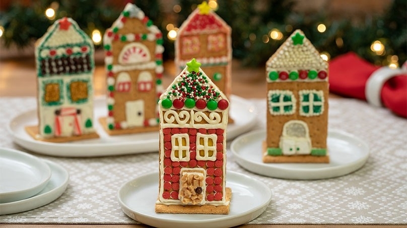 Easy Honey Made Holiday Houses on white plates, red napkin, woven placemat, holiday garland with white lights, wood tabletop