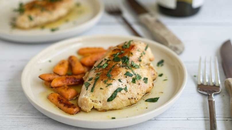 White Wine and Honey Glazed Chicken with carrots, white plates, knives and forks, light wood table