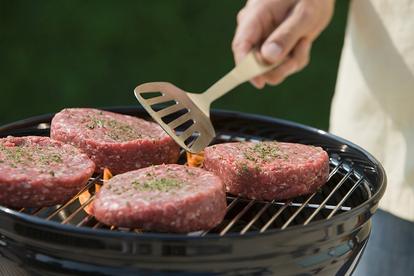 Hand flipping burger patties on grill with metal spatula