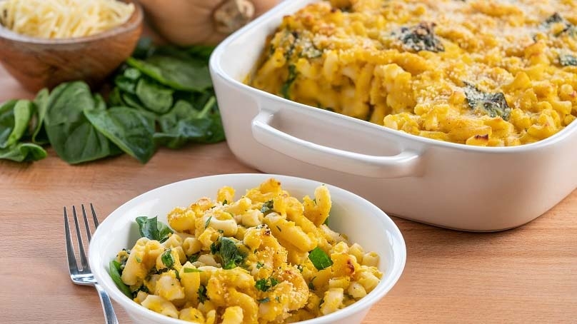 Baked Butternut Squash Mac & Cheese in bowl, casserole dish, bowl of shredded cheese, fresh garnish, fork, wood table